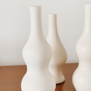 Three tall white and thin vases with a pear shape that has a flute opening at the top